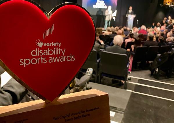 Image of the heart shaped variety disability sport award trophy in the foreground, with the stage blurred in the background.