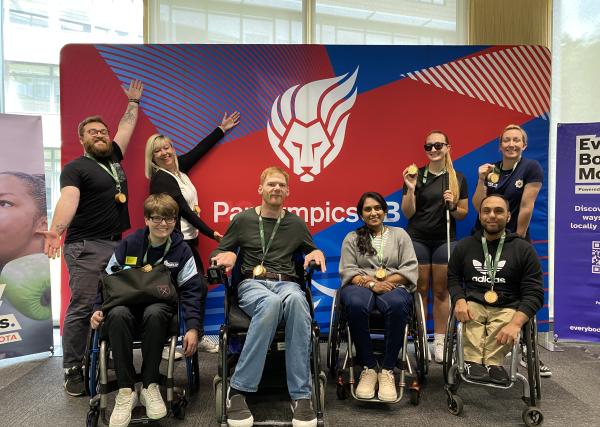 The LAB at kitting out are pictured smiling with their arms up infront of a Paris ParalympicsGB branded backdrop.