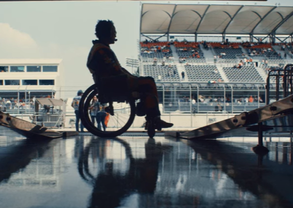 Silhouetted wheelchair user, framed side on, in the garage entry of a pit lane at a race track