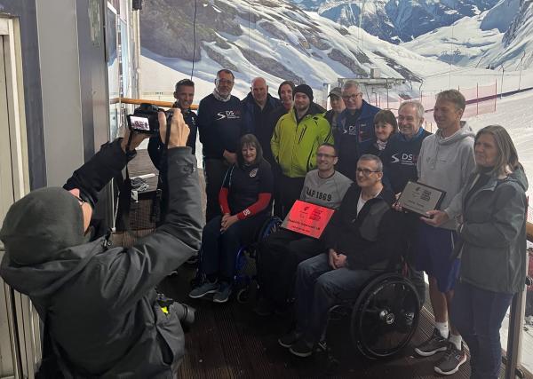 Club of the year 2024 winners DSUK, with club members on a balcony overlooking an indoor ski slope. Trophy in the middle of shot, with all looking towards a photographer taking a photo of them.