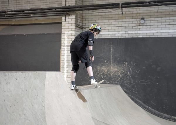 adaptive skateboarder in helmet and pads, getting ready to drop in on a quarter pipe