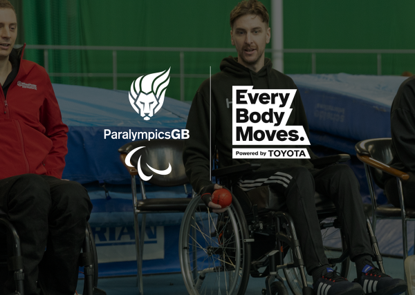 A white ParalympicsGB Lion logo with Agitos adjacent to a white Every Body Moves powered by Toyota logo. This logo lock up is embossed over a game of Boccia in a large sports hall with three seated players looking on.