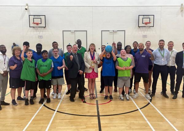 Croydon RAP disability sport programme Club of the Month Award handover event. Image show a range of staff and participants in a line across an indoor basketball court, smiling and looking towards the camera, with award held in the middle of shot.