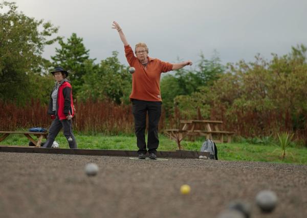Petanque player stood and mid throw, with ball heading towards camera
