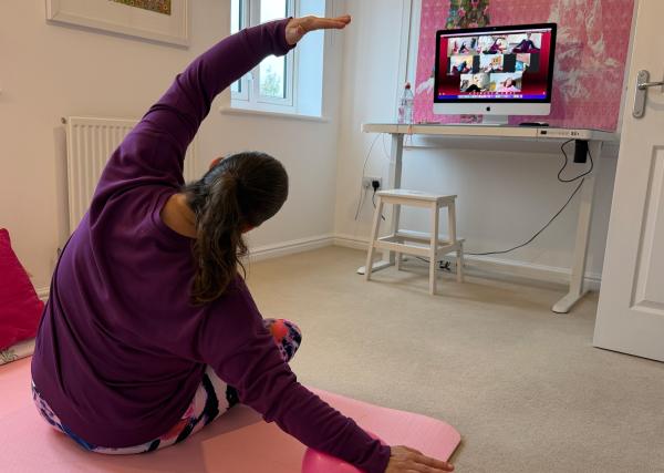 Instructor delivering an online adaptive pilates session - sat on the floor facing away from the camera with computer screen in front of them